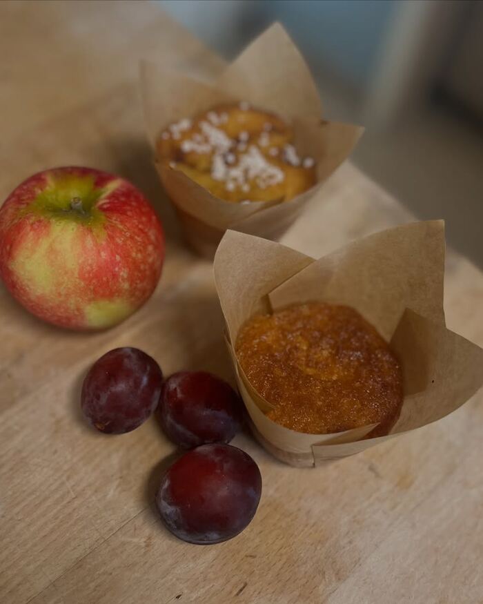 To cupcakes i papirform med fruktfyll, ved siden av et eple og noen plommer.