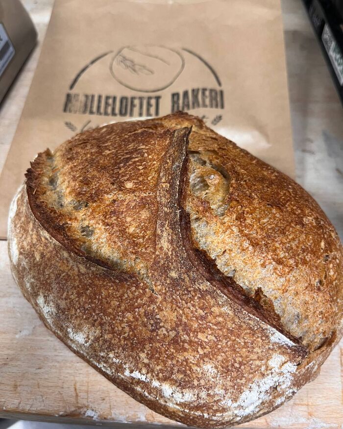 Surdeigsbrød med sprø skorpe på en papirpose med logoen til Mølleloftet bakeri.